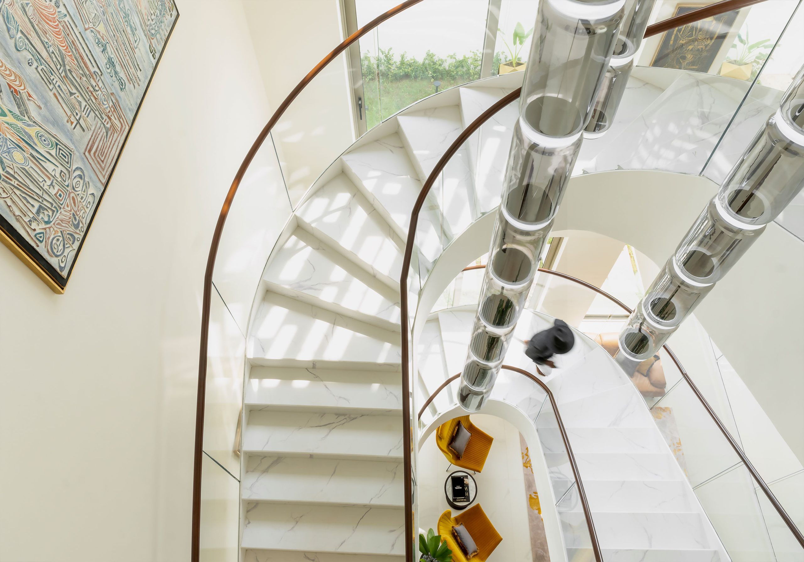 An aerial view of a luxurious staircase with a modern, artistic railing and white marble steps, designed by the leading architectural design studio in Lagos, Oshinowo Studio, led by Tosin Oshinowo, featuring a spacious and bright interior with contemporary furnishings and a large, colorful wall art piece.
